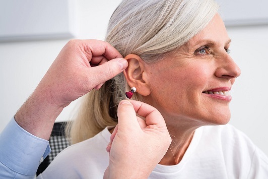 Eine Seniorin bekommt ein modernes Hörgerät angepasst und lächelt zufrieden.